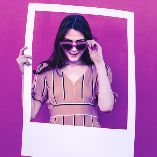 Woman holding a white VIP Services - Premier picture frame, smiling behind Socially Inclined sunglasses optimized for social media marketing, against a purple background.